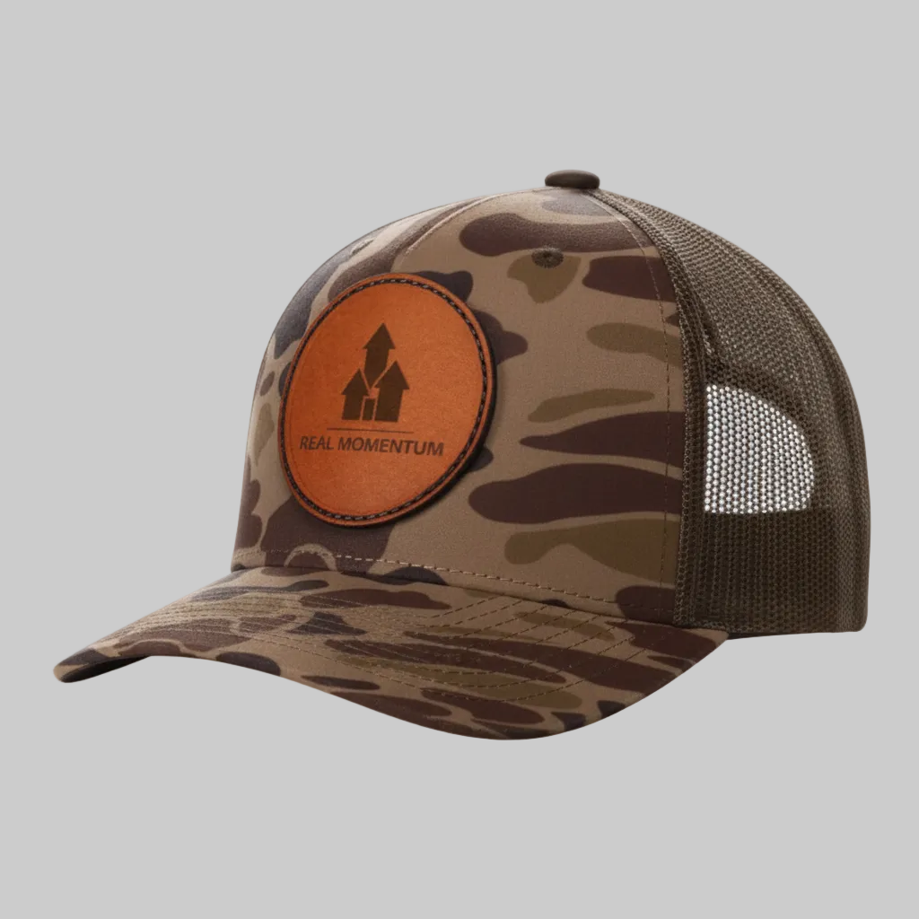 Camouflage cap with a brown patch featuring 'Real Momentum' logo on a white background
